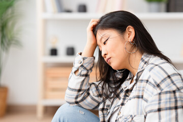 Sad and pensive woman sitting at home leaning her head on hand