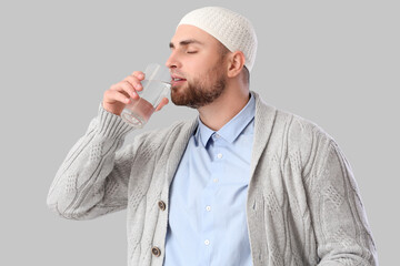 Young Muslim man drinking water on light background. Ramadan celebration