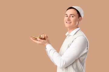 Young Muslim man with Aladdin lamp on beige background. Ramadan celebration