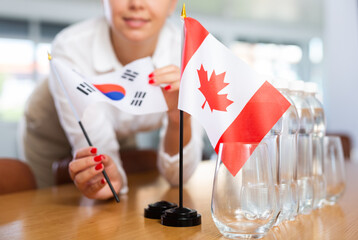 Young woman in business clothes puts flags of South Korea and Canada on negotiating table in...