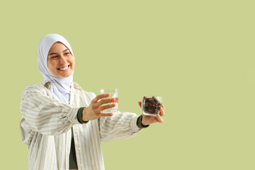 Young Muslim woman with dates and glass of water on green background. Ramadan celebration