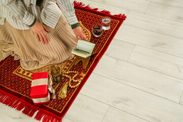 Young Muslim woman with Koran on mat, closeup. Ramadan celebration