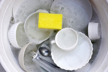 Dirty dishes with cleaning sponge in foam of dishwashing liquid. Washing dishes concept
