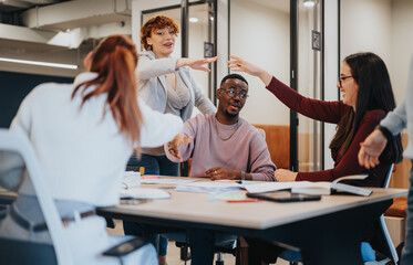 Colleagues celebrating a finished project in the office, happy and overjoyed with successful outcomes. Businesswoman and multicultural coworkers caught up in the joy of winning achievements.