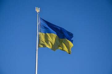 National Ukrainian flag on a flagpole with a trident blowing in the wind against a clear blue sky