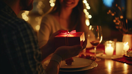 Obraz na płótnie Canvas Husband or Boyfriend Holding Red Gift Box in Hands, Making Present Surprise to Happy Girlfriend Wife Having a Romantic Dinner Date in Candlelight, Close Up. Couple Celebrates Valentine's Day on Februa