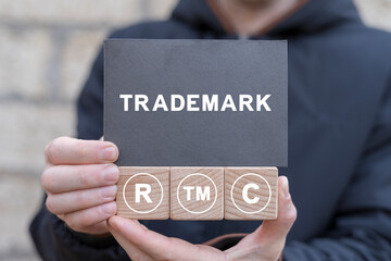 Man holding wooden cubes with icons and black sticky note with word: TRADEMARK. Trademark TM...