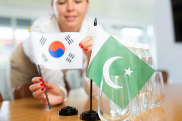 Positive young woman putting little flag of South Korea on table next to the flag of Pakistan and...