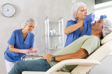 Adult man undergoing botulinum therapy session at aesthetic medicine clinic. Skilled woman...