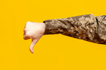 hand of a male soldier of the Ukrainian army in camouflage pixel uniform shows dislike and thumbs...