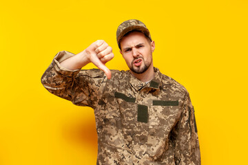 young Ukrainian male soldier in camouflage pixel uniform shows dislike and thumbs down on a yellow...