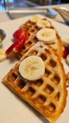 beautiful golden brown waffles covered in strawberries and banana slices with butter and syrup on a plate in Pasadena California USA