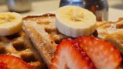 beautiful golden brown waffles covered in strawberries and banana slices with butter and syrup on a plate in Pasadena California USA