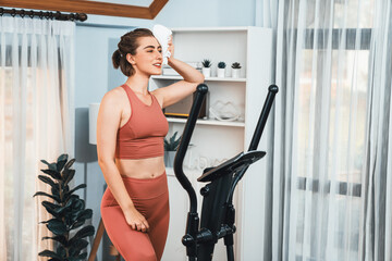 Athletic and sporty woman running on elliptical running machine during home body workout exercise session for fit physique and healthy sport lifestyle at home. Gaiety home exercise workout training.