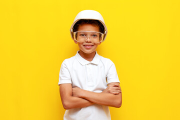 african american boy builder repairman in hard hat and safety glasses stands with crossed arms on...