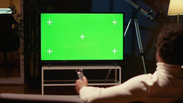 Man using remote to zap through films available on streaming services on mockup TV. Person having movie night in home theatre using isolated screen television set, relaxing on couch