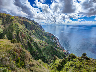 Fototapeta na wymiar Scenic view over Paul do Mar village at the west coast of Madeira Island. Green mountains, roads, blue ocean and sky with white clouds landscape