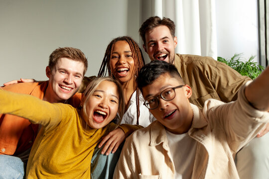 multiracial group of young friends smiling and taking selfies for the camera, asian, african american and european students hugging and taking pictures together