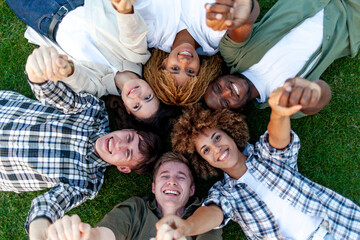 group of multiracial young people relax and lie together on the grass in the park and smile, team...