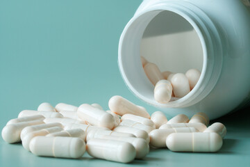 White medical capsules next to open container - bottle on pastel green-blue background. Photo