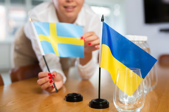 Preparation for international negotiations of partners on European integration path. Female office coordinator setting national flags of Ukraine and Sweden on table, selective focus..