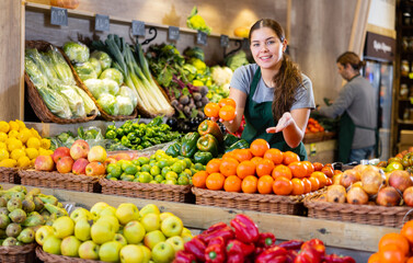 Saleswoman near fruit and vegetables stalls offering to buy mandarin oranges