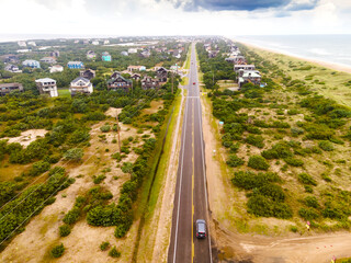 road through a small town in America along the ocean filmed from a drone. Houses, trees, cars.