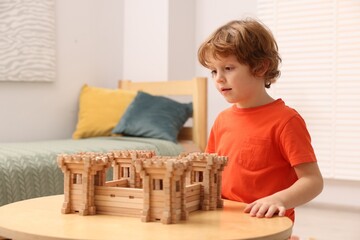 Fototapeta na wymiar Cute little boy playing with wooden fortress at table in room. Child's toy