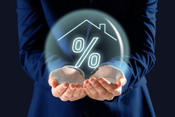 Mortgage. Man holding sphere with percent sign and house roof on dark blue background, closeup