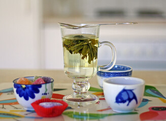 Tea time. Glass of flowering tea, mochi cake, gummies on the place mat with birds pattern