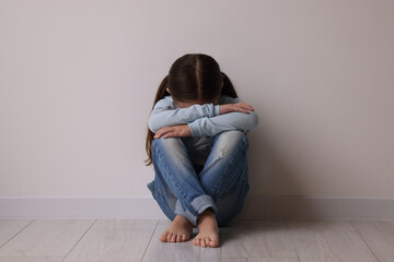 Child abuse. Upset little girl sitting on floor near light wall indoors - obrazy, fototapety, plakaty