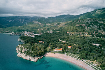 Fototapeta na wymiar Beach and green park near Villa Milocer at the foot of the mountains. Montenegro. Top view