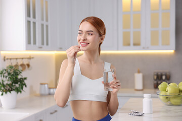 Young woman with glass of water taking pill in kitchen. Weight loss