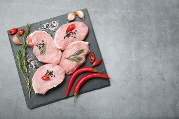 Pieces of raw pork meat, chili peppers and spices on grey table, top view. Space for text