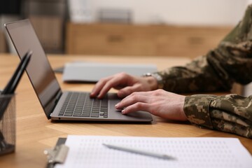 Military service. Soldier working with laptop at wooden table indoors, closeup