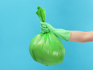 Woman holding plastic bag full of garbage on light blue background, closeup. Space for text