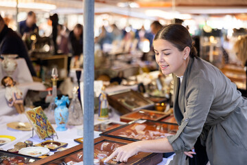 Fototapeta na wymiar Satisfied interested young woman choosing interesting antique things at traditional flea market