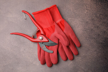 Pair of red gardening gloves and secateurs on brown textured table, top view