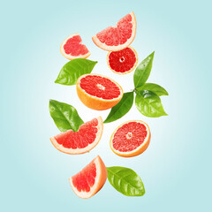 Fresh grapefruit pieces and green leaves falling on light blue background
