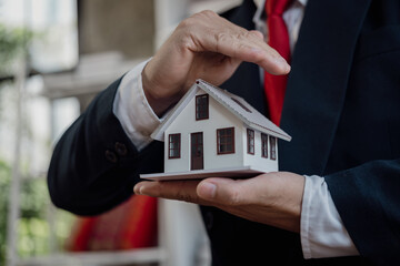 A businessman in a suit holds a house model in the palm of his hand. Mortgage Lending Concepts Real...