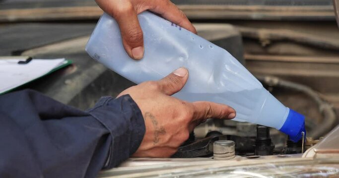 Car Mechanic man hands pouring Deionized purified Distilled water for car battery mechanical service. Close up hands man hold Deionized Distilled liquid water bottle at garage auto mobile car service