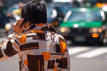 People wearing fashion shirt and having a call on cellphone in foreground, taxis in background, Tokyo, Japan