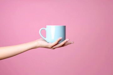 Female hand holding blank coffee cup for mockup on palm over pink background 