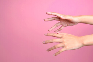 Two female's hands trying to grab or reach something isolated over pink background - obrazy, fototapety, plakaty