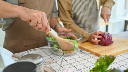 Senior couple in aprons preparing a fresh healthy vegan salad in kitchen. Healthy eating and...