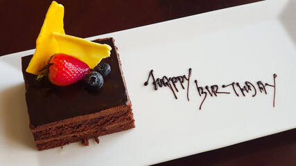 Birthday dessert. Piece of cake with strawberries lies on plate. Happy birthday inscription with chocolate.