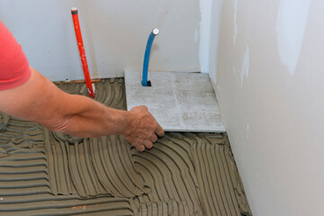 On bathroom floor tiler is placing ceramic tiles over adhesive