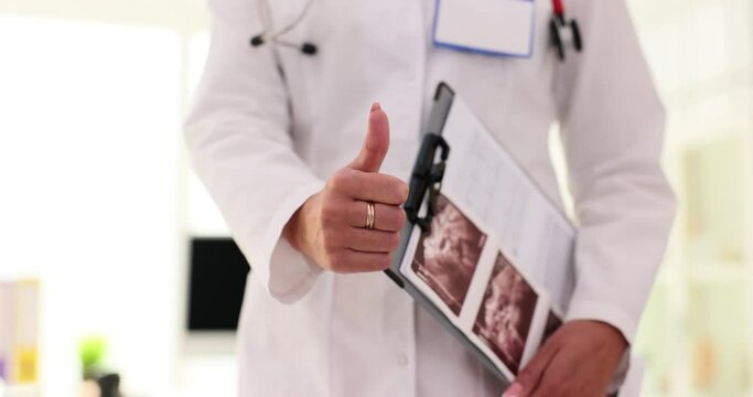 Female doctor shows thumb up holding clipboard with US image