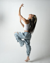 Full length portrait of brunette female asian model wearing casual clothes, white singlet shirt, denim jean pants.  Energetic jumping, dancing pose. Isolated on white studio background.