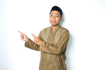 calm asian muslim man smiling at camera wearing koko clothes pointing to beside isolated on white...